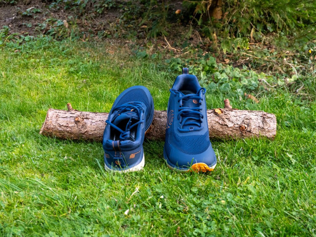 Ein Paar blaue Topo Athletic Terraventure 5 von vorn, an einen Holzstamm gelehnt